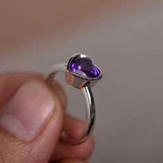 a close up of a person holding a ring with a purple stone in the middle