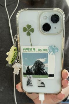 a person holding up a cell phone case with pictures on it and a green leaf attached to the back