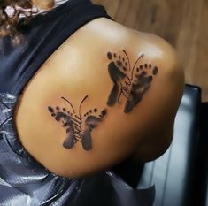 the back of a woman's shoulder with two footprints and butterflies tattooed on it