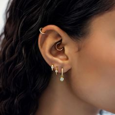 a woman wearing gold ear cuffs with small green stones on the end of each ear