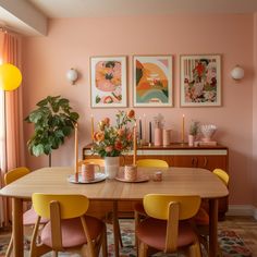 a dining room table with yellow chairs and pink walls in front of it, along with pictures on the wall