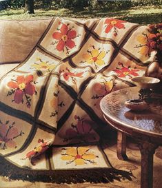 a couch with a blanket on top of it next to a table and flower vase