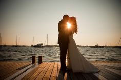 a bride and groom kissing on a dock at sunset