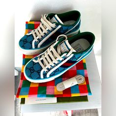 two blue sneakers are sitting on top of a colorful table cloth with an electronic device