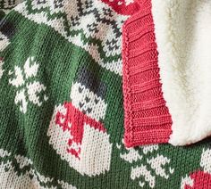 a green and red knitted blanket laying on top of a white tablecloth covered in snowflakes