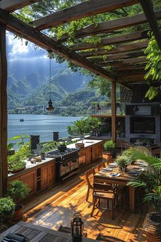 an outdoor kitchen and dining area overlooks the water with mountains in the back ground