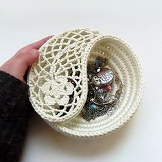 a hand holding a small white basket with jewelry in it