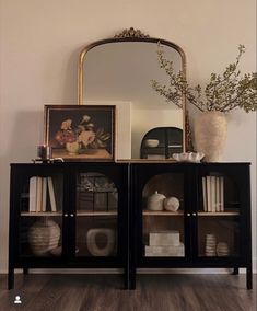 a black bookcase with books, vases and pictures on it in front of a mirror