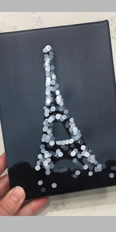 a hand holding up a black and white canvas with the eiffel tower painted on it