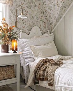 a white bed sitting under a window next to a table with flowers on top of it