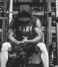 a man sitting on top of a bench in front of a gym equipment rack wearing a hoodie