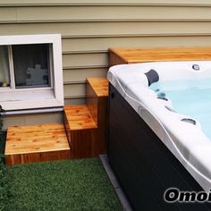 a hot tub sitting in the grass next to a wooden step leading up to a window