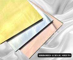 three sheets of colored paper sitting next to each other on a white satin sheeting