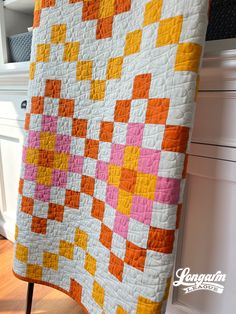 an orange, pink and yellow quilt hanging on a white wall next to a cabinet