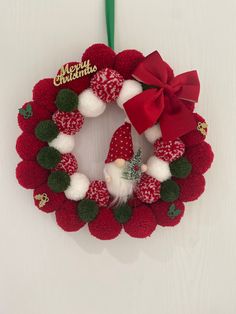 a red and white christmas wreath with pom - poms hanging on a green ribbon