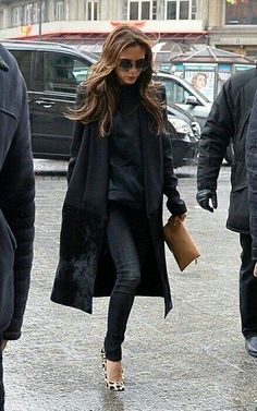 a woman in black coat and leopard print shoes walking down the street with other people