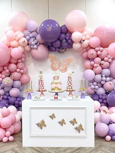 a table topped with lots of balloons next to a wall covered in pink and purple