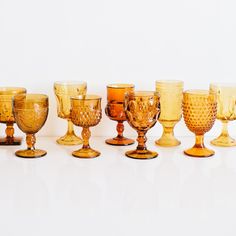 an assortment of glass goblets are lined up on a white surface, including one in the middle