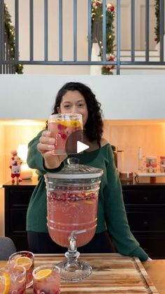 a woman holding up a drink in front of a table with fruit and drinks on it