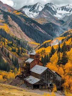 an old building in the mountains with yellow trees and snow capped mountains behind it on a cloudy day