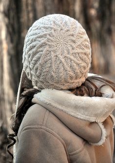 a woman wearing a white hat and coat in front of some trees with her back to the camera