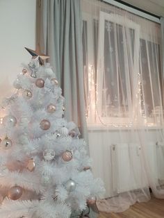 a white christmas tree with gold and silver ornaments in front of a curtained window