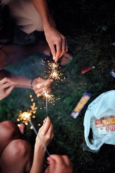 people are sitting on the grass and holding sparklers