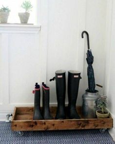 four pairs of rain boots and an umbrella on a wooden tray in front of a door