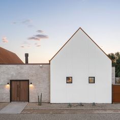 a white house with two doors and windows on the outside, along side a brick wall