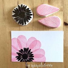 some pink and black flowers are on a wooden table next to two rubber stamps, one with a flower