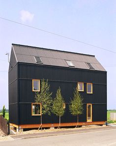 a black building with three windows and two trees on the side of it, in front of an empty street