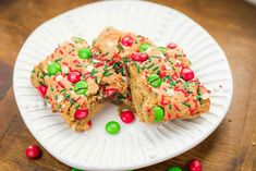 a white plate topped with pieces of cake next to green and red candies on top of a wooden table