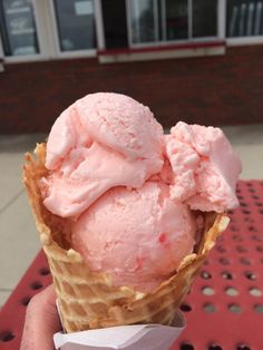 a hand holding an ice cream cone with pink icing