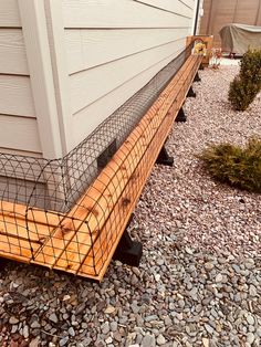 a wooden bench sitting on top of a gravel covered ground next to a building with a wire fence around it