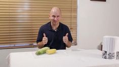 a bald man sitting at a table giving the thumbs up sign and holding a banana