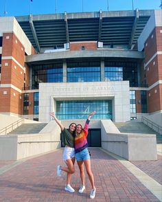 two girls are posing in front of the university of alabama building with their arms up