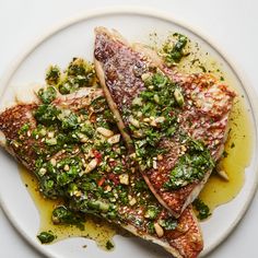 two pieces of fish on a plate covered in pesto and pine nut toppings