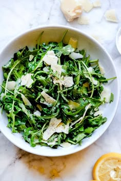 a white bowl filled with green salad next to sliced lemons and parmesan cheese