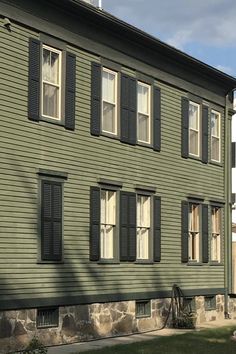 a large green house with black shutters on the front and side windows, sitting next to a grassy lawn