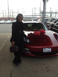 a woman standing next to a red car with a large bow on it's hood