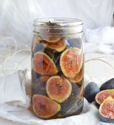 figs and other fruits are in a jar on a white cloth next to some fruit