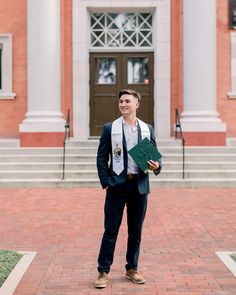 a man standing in front of a building holding a green book and smiling at the camera