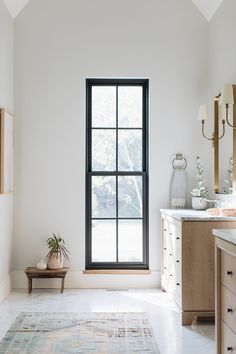 a white bathroom with a large window and rug on the floor in front of it