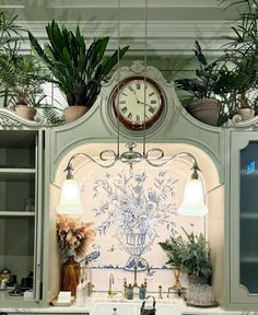 a kitchen sink under a clock with potted plants