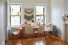 a dining room table with four chairs and a rug hanging from the ceiling in front of two windows