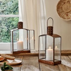 three lit candles are sitting on a wooden table next to bread and other items in front of a window