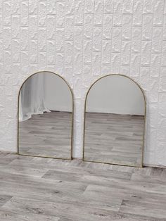 two mirrors sitting next to each other on top of a wooden floor in front of a white wall