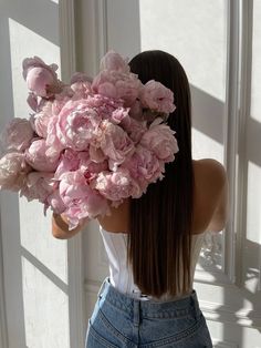 a woman holding a bunch of pink flowers in front of her face and back to the camera