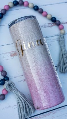 a pink and silver glitter tumbler with the word finn on it next to tassels