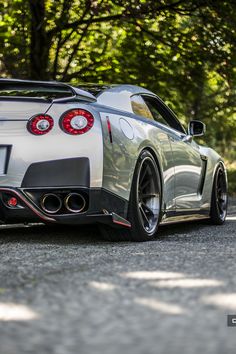 the rear end of a white sports car parked in front of some trees and bushes